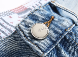 Macro shot of a silver metal button with JEANS text on distressed blue denim shorts