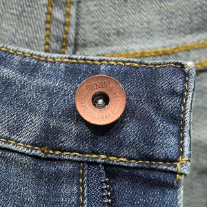 Macro shot of bronze metal button with DENIM engraving on blue denim shorts
