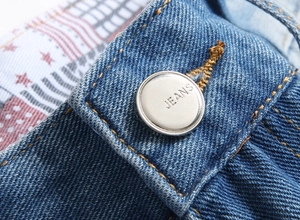 Macro detail of silver jeans button with star-spangled banner lining on denim shorts