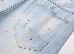 Macro view of light blue denim fabric with colorful paint splatter on the back pocket