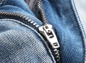 Close-up of durable silver metal zipper on light blue distressed denim shorts for men