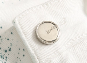 Gros plan d'un bouton argenté gravé Jeans avec des taches de peinture sur denim blanc