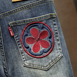 Detailed close-up of premium carp embroidery on deep blue washed denim shorts