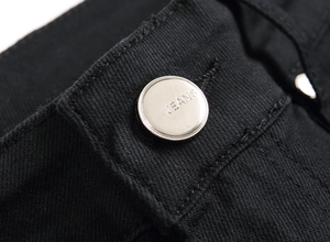 Detail of silver metal button with JEANS engraving on black denim fabric texture