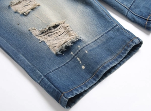 Detail of distressed blue denim jeans showing ripped holes and white paint splatter design