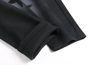 Detailed close-up of the double-stitched hem and grey star print on black denim jeans