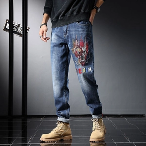 Détail d'un jean bleu délavé avec une broderie de dragon complexe et un texte denim