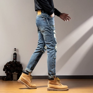 Detail of distressed ripped jeans featuring heavy washing and vintage leather brand patch
