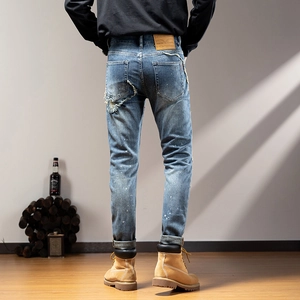 Detail of ripped blue slim-fit jeans with white paint splatters and back pocket embroidery