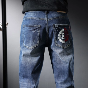 Détail de jean bleu homme avec broderie rouge et blanche sur la poche arrière