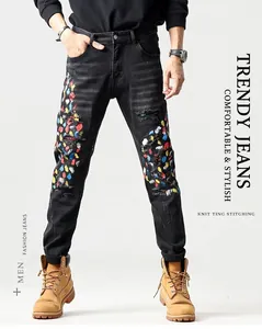 Detail van heren slim jeans in zwart met kleurrijke verfspatten en distressed patches