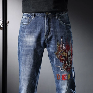 Détail de la broderie lourde de dragon et crâne sur le jean en denim bleu