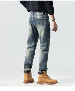 Detail showing vintage wash denim texture and leather waist label on slim straight jeans