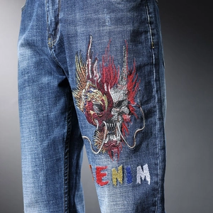 Gros plan sur la broderie de dragon et le texte Denim sur un jean bleu délavé