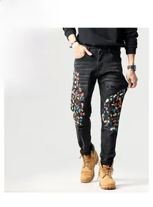 Detail van een zwarte slim jeans met kleurrijke verfspatten en modieuze scheureffecten