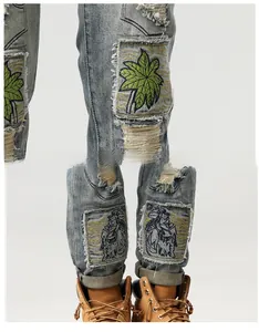 Dettaglio dei jeans azzurri strappati con ricamo di palma verde e toppe in stile retrò