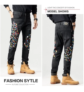 Detail van slim fit zwarte jeans met kleurrijke verfspatten en distressed accenten