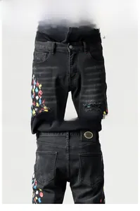 Detail van de zwarte slim-fit spijkerbroek met distressed patches en verfspatten