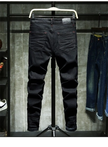 Close-up of black slim fit jeans featuring red contrast stitching and pleated pocket detail