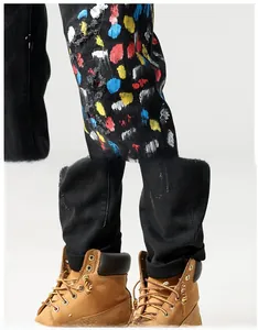 Detail van zwarte distressed denim broek met kleurrijke verfspatten en scheuren