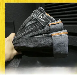 Detail of slim fit washed black jeans featuring orange contrast stitching and metal button