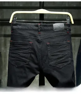 Detail view of black denim pants with red contrast stitching and leather brand patch