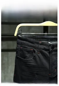 Detail view of black denim jeans featuring contrasting red stitching and metal waist button