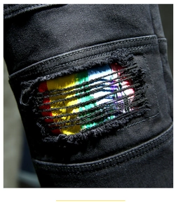 Macro detail of black distressed denim jeans featuring vibrant rainbow stripe patchwork