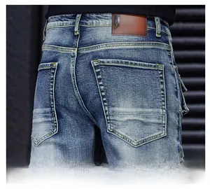 Close-up of men's blue distressed denim jeans showing the leather brand label and pocket detail