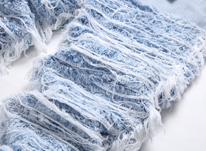 Close-up of heavy distressed ripped denim texture with white frayed fiber details