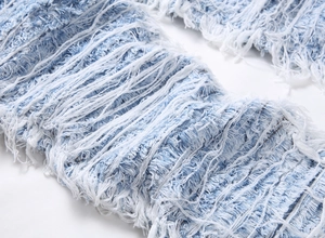 Macro detail of distressed denim fabric with heavy fringe embroidery and frayed textures