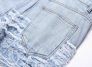 Close-up of light blue denim with heavy distressed frayed tassel details and pocket texture