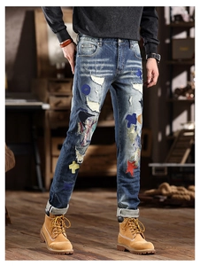 Detail view of slim fit blue denim jeans with colorful embroidery patches and ripped design