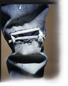 Détail d'un jean bleu vintage coupe slim avec des trous usés et des taches de peinture