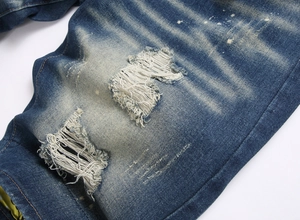 Detailed macro view of distressed dark blue denim with rip design and white paint splashes
