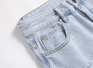 Detail of light blue denim waist with metal button and reinforced stitching details