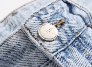 Macro shot of silver metal button with JEANS engraving on light blue washed denim fabric