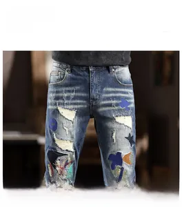 Detail of street style light blue denim jeans with embroidery patches and ripped holes