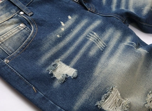 Macro detail of distressed denim shorts with whiskering, silver rivets, and ripped effects