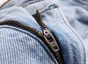 Detailed close-up of a premium bronze metal zipper on light blue distressed denim jeans