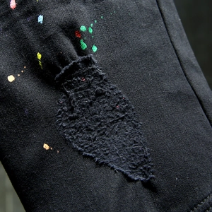 Distressed black denim jeans with colorful paint splatter and ripped details, 2025 style