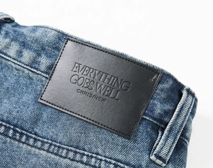 Macro shot of the black leather brand patch with embossed letters on light blue denim jeans