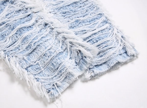 Macro detail of heavy embroidery fringe and distressed frayed hems on light blue denim
