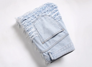 Detail showing distressed ripped fringe and washed denim texture on men's streetwear jeans