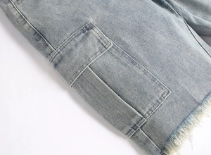 Detail of light blue denim fabric featuring workwear cargo pockets and frayed tassel hems