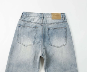 Dettaglio di jeans blu con etichetta in pelle marrone e cucitura ondulata sulla tasca
