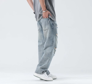 Detailed view of light blue washed denim with distressed rips and fashion label on back pocket