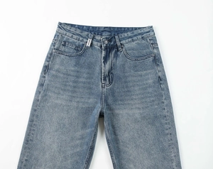 Detail view of light blue washed denim jeans featuring a metal button and branded woven label
