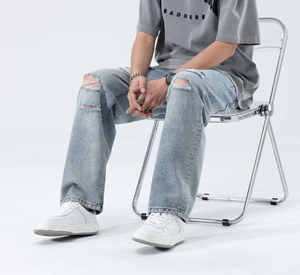 Detail of light blue washed denim jeans with distressed knee holes on a male model
