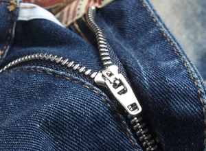 Detail shot of the metal zipper and orange stitching on blue denim shorts for men